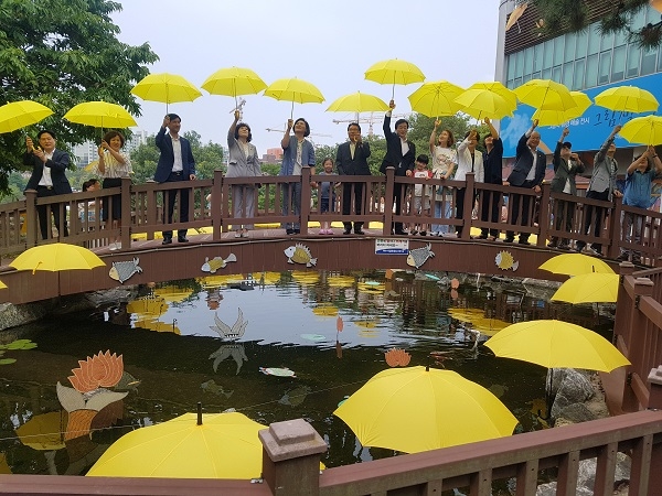 ▲15일 환경도서관 스페이스 갤러리 개관식 참여자들이 연못앞에서 노란우산을 펼쳐들고 있다. 가운데 권오봉 여수시장